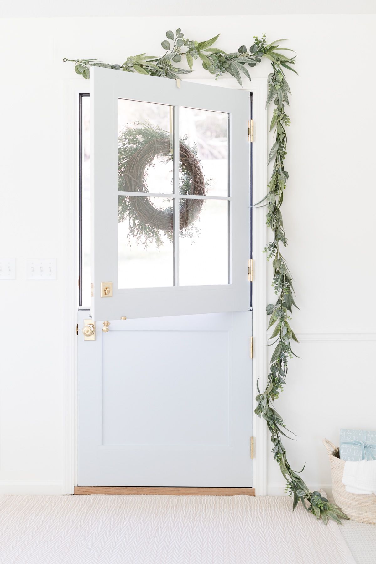 A blue dutch door decorated with a garland for a coastal Christmas decorating look