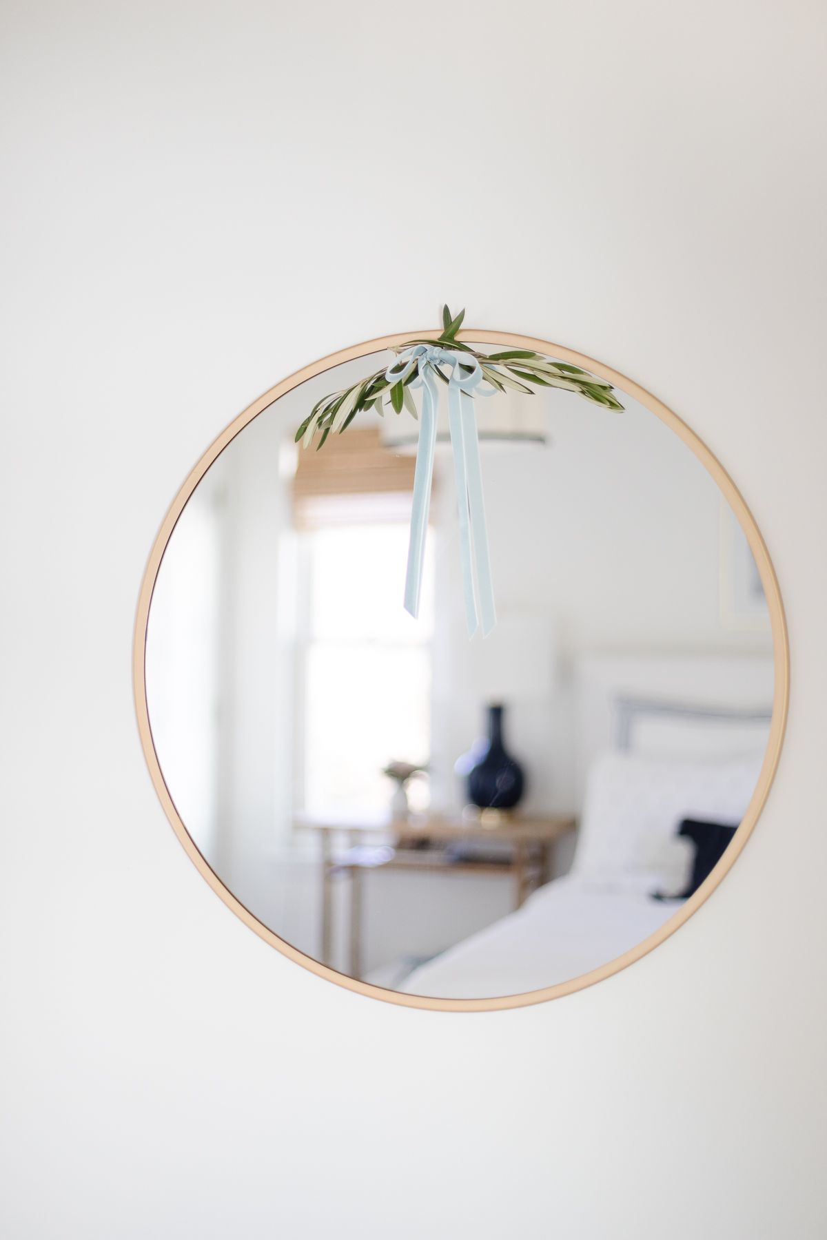 A round brass mirror accented with fresh holiday greenery and a blue velvet bow