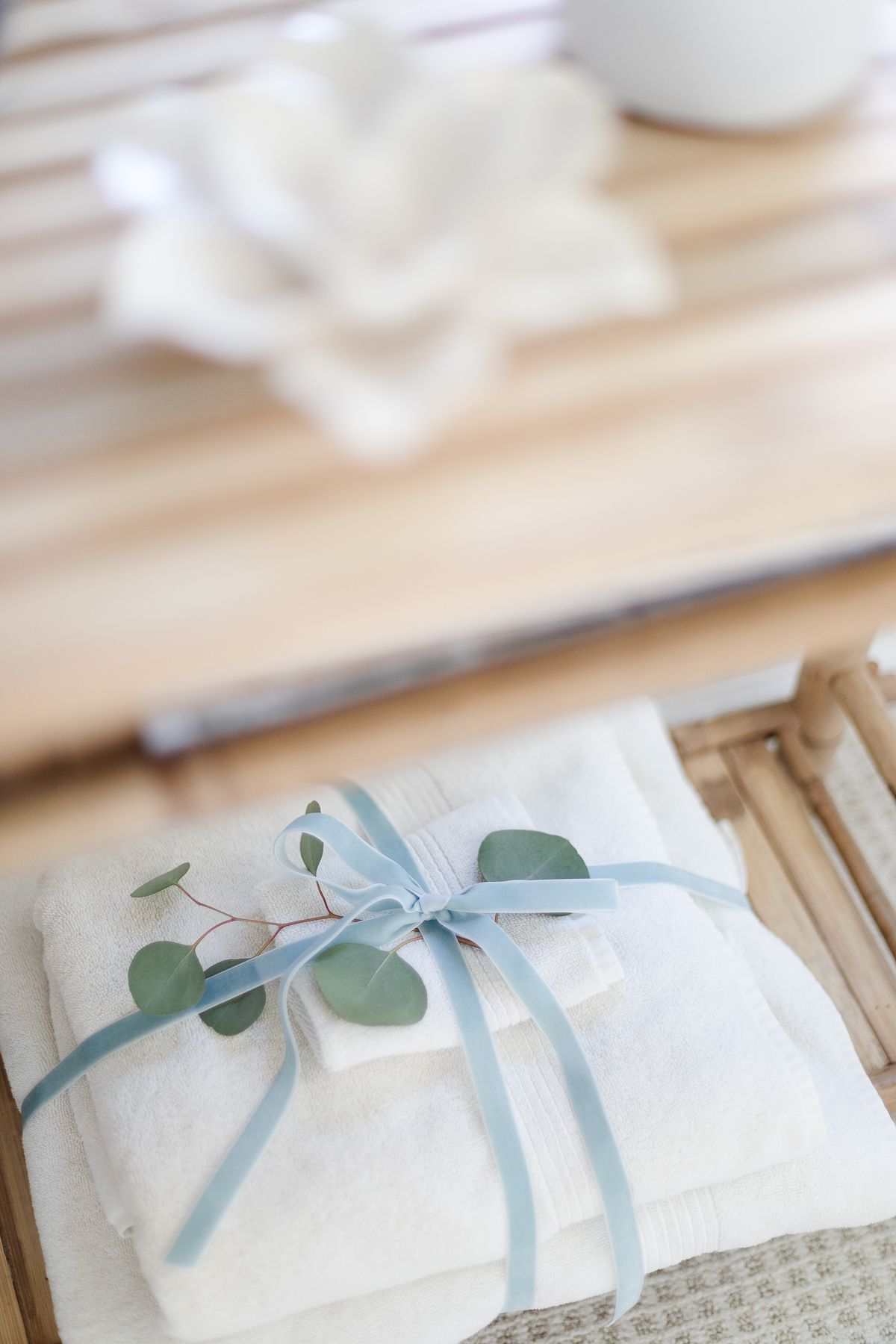 A stack of white towels in a guest room, accented with greenery and a velvet bow for coastal Christmas style.