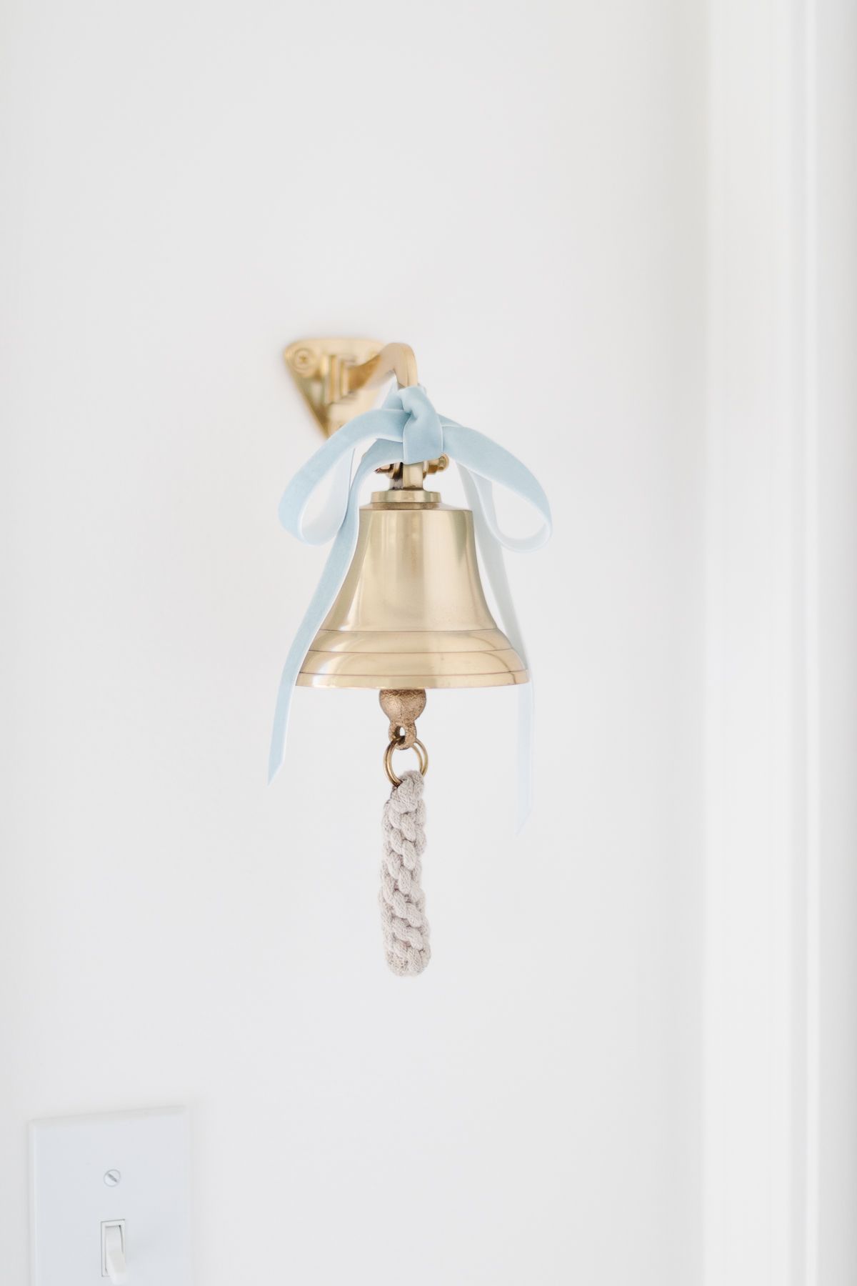 A brass bell on a white wall, tied with a blue velvet bow.