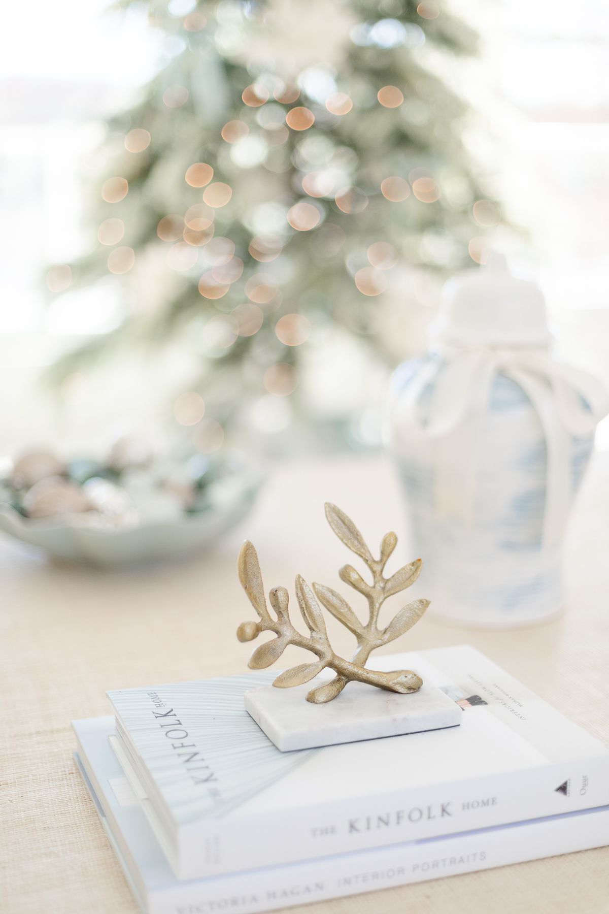A brass mistletoe accent on a stack of books with a coastal Christmas tree in the background.