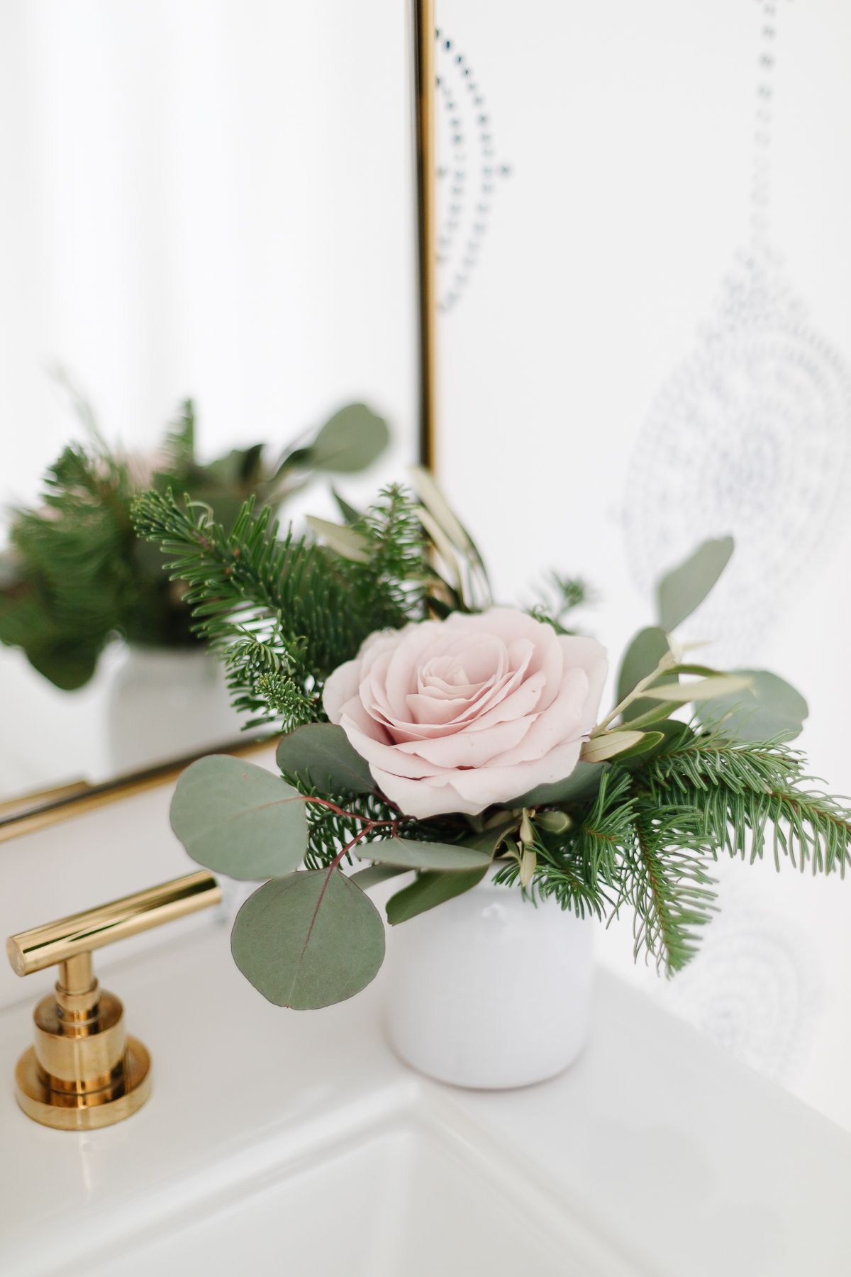 A small vase of holiday greenery and a soft pink rose in a coastal Christmas bathroom.