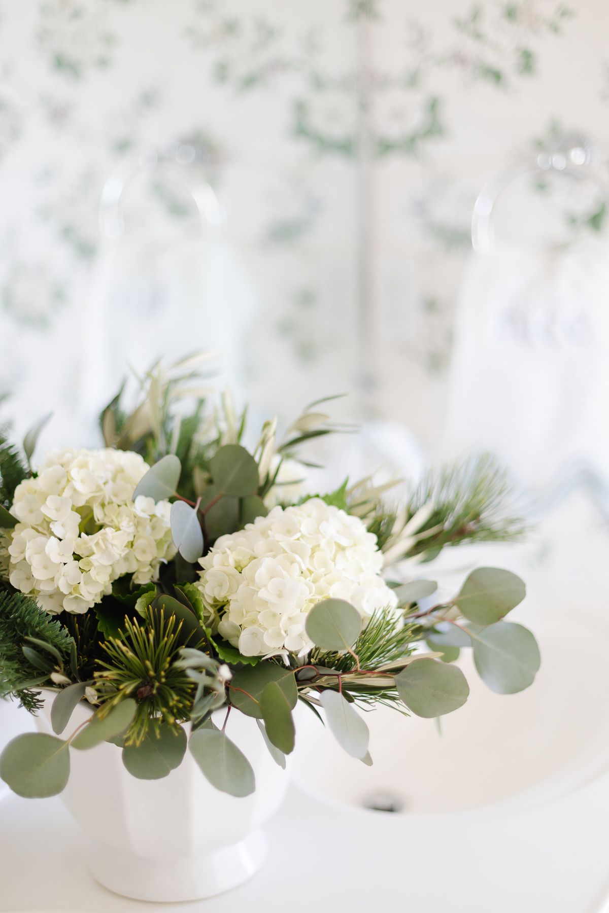 A coastal Christmas green and white coastal Christmas arrangement in a floral wallpapered bath.