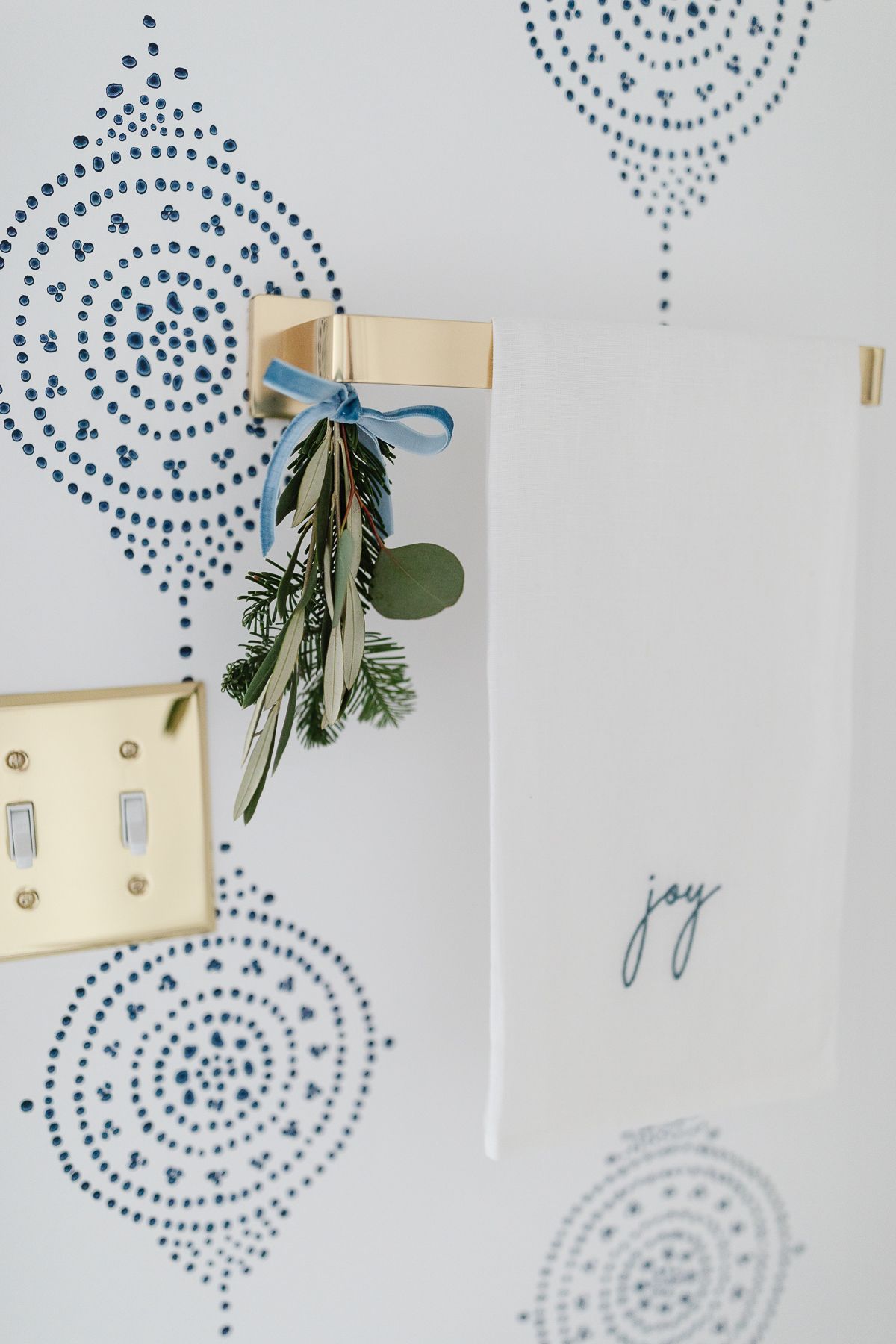 Touches of holiday greenery tied onto a brass towel rack in a coastal bathroom.