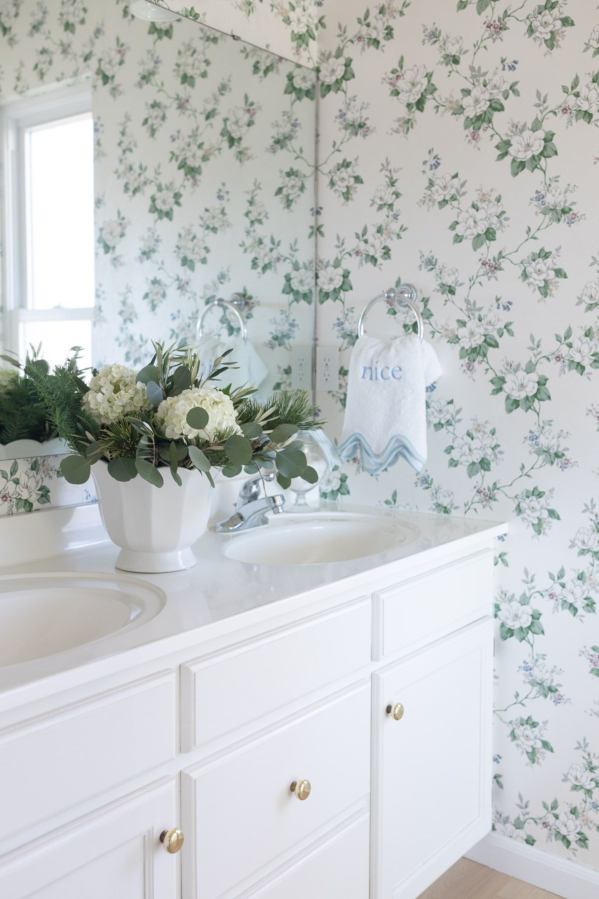 A coastal Christmas green and white coastal Christmas arrangement in a floral wallpapered bath.