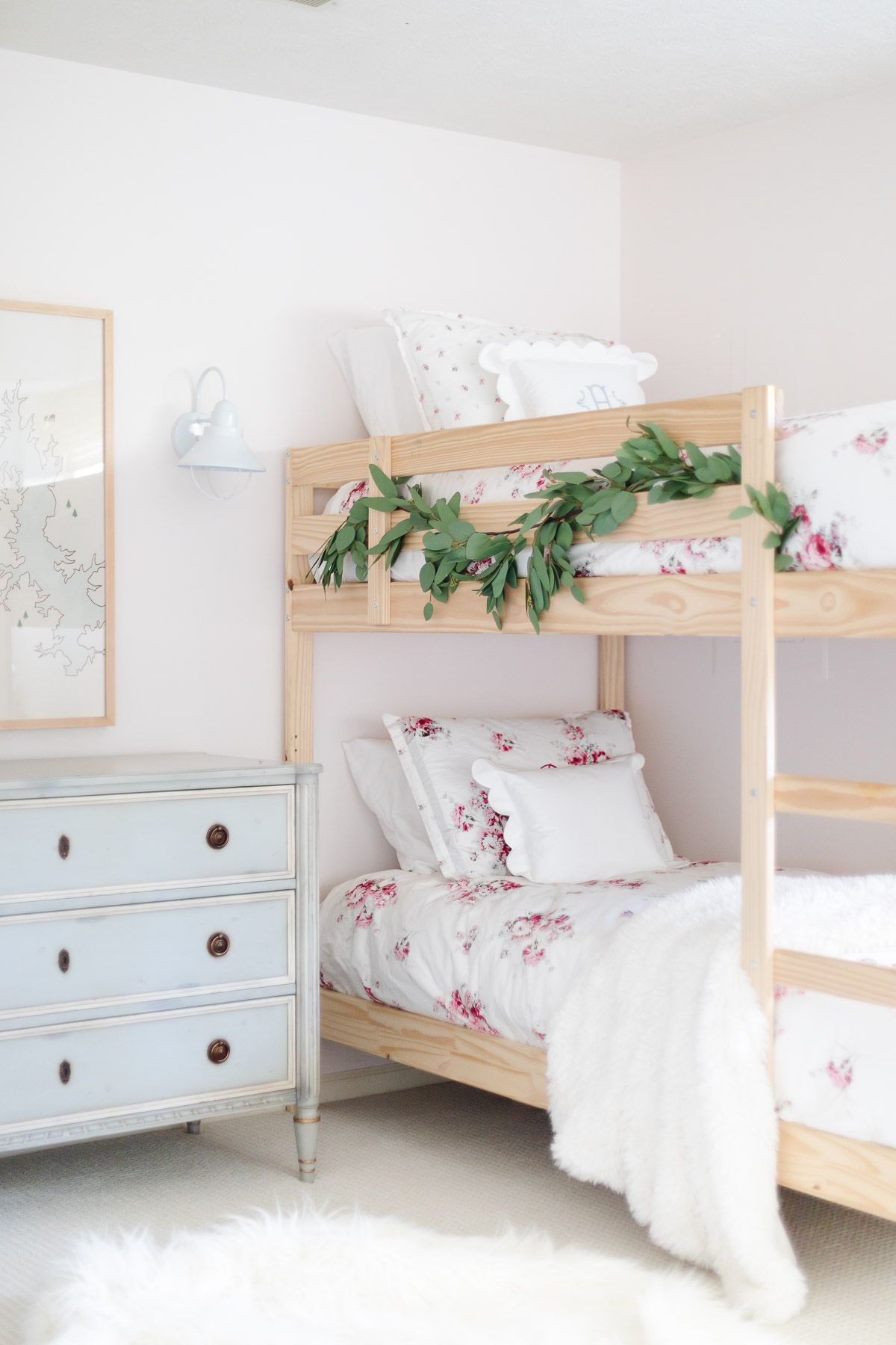 A bedroom with wooden bunk beds and floral bedding, decorated with garland for a coastal Christmas look.