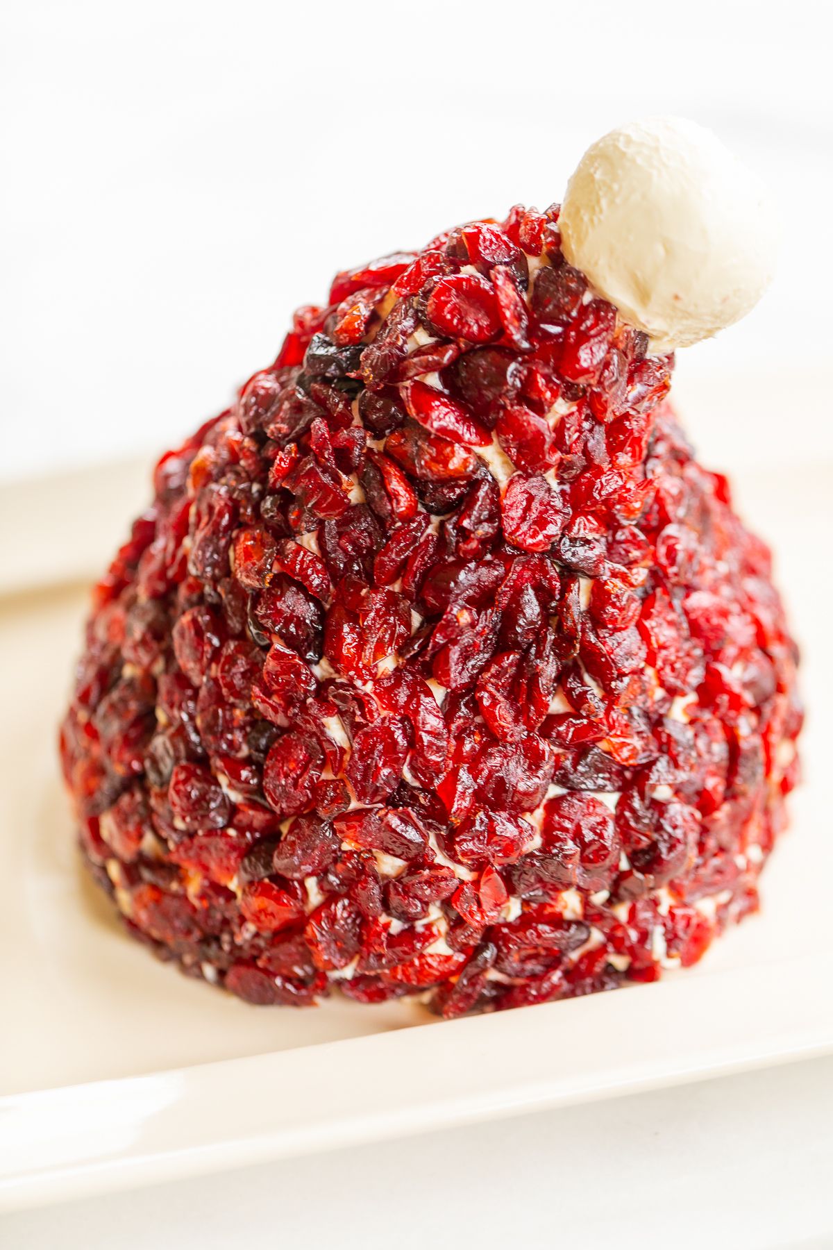 A cranberry cheeseball in the shape of a Santa's hat, on a white plate.
