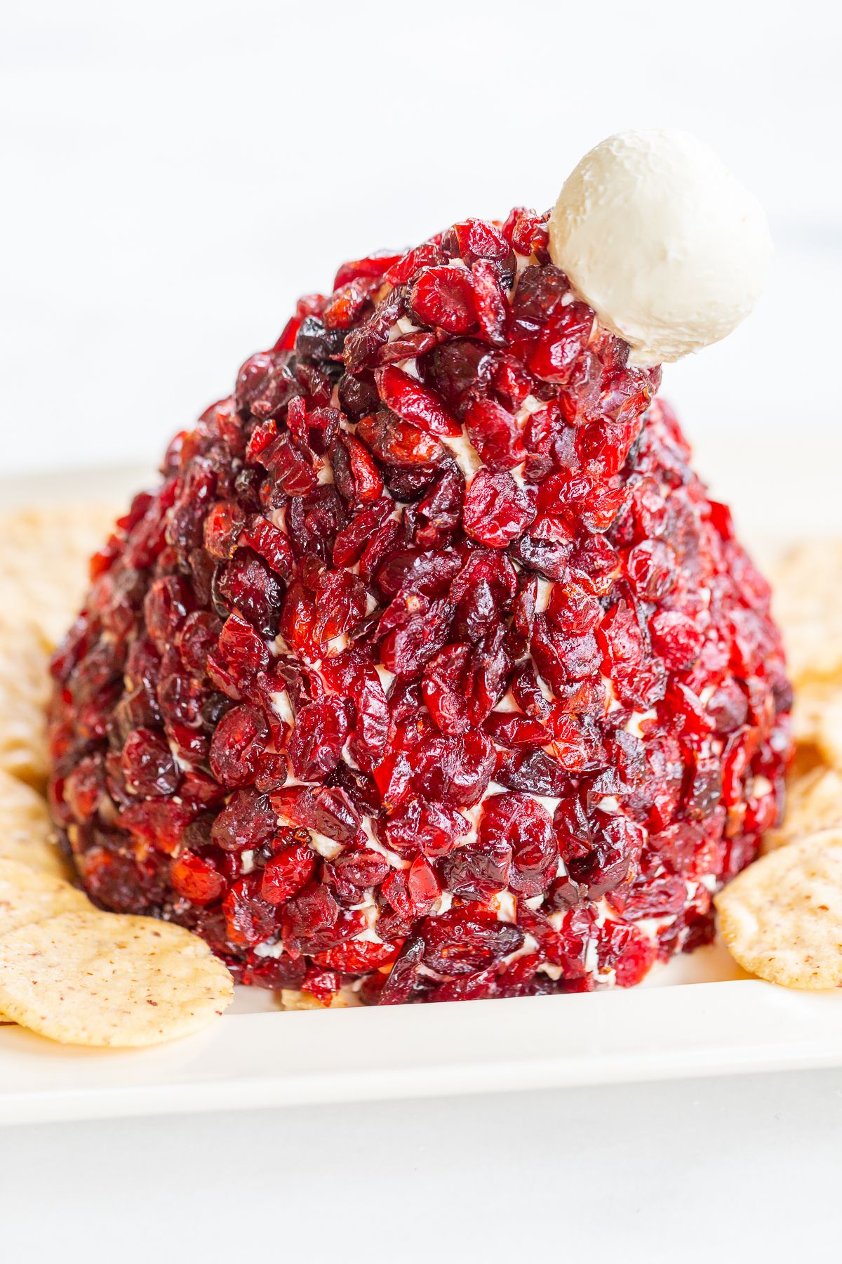 A cranberry cheeseball in the shape of a Santa's hat, on a plate surrounded by crackers.