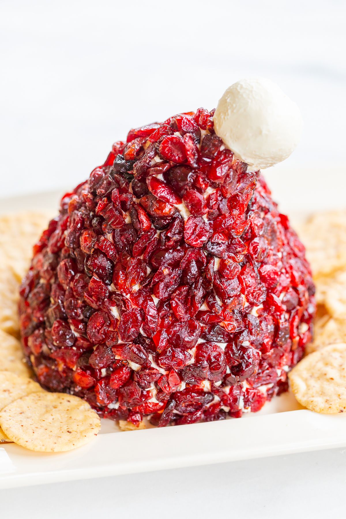 A cranberry cheeseball in the shape of a Santa's hat, on a plate surrounded by crackers.