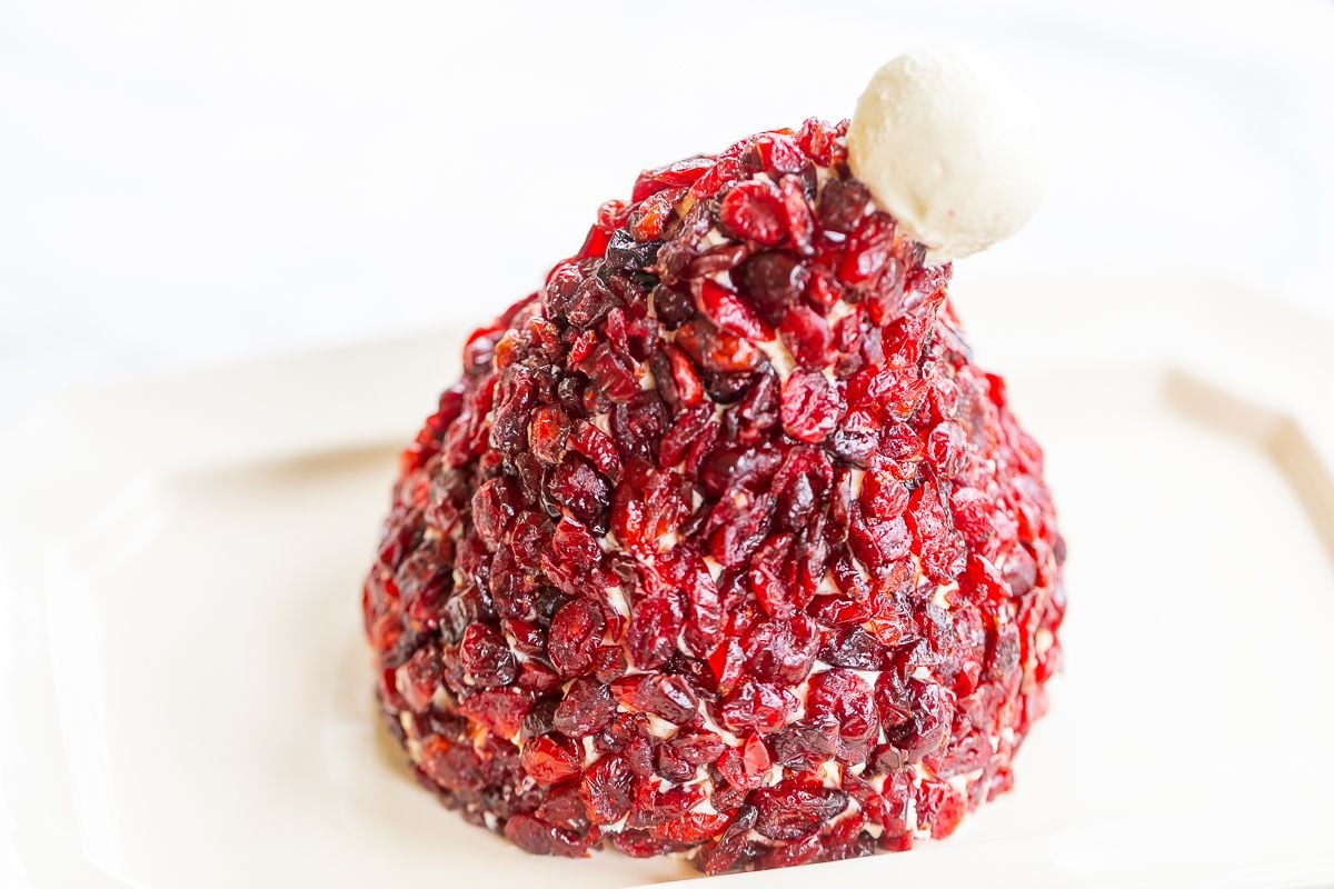 A cranberry cheeseball in the shape of a Santa's hat, on a white plate.