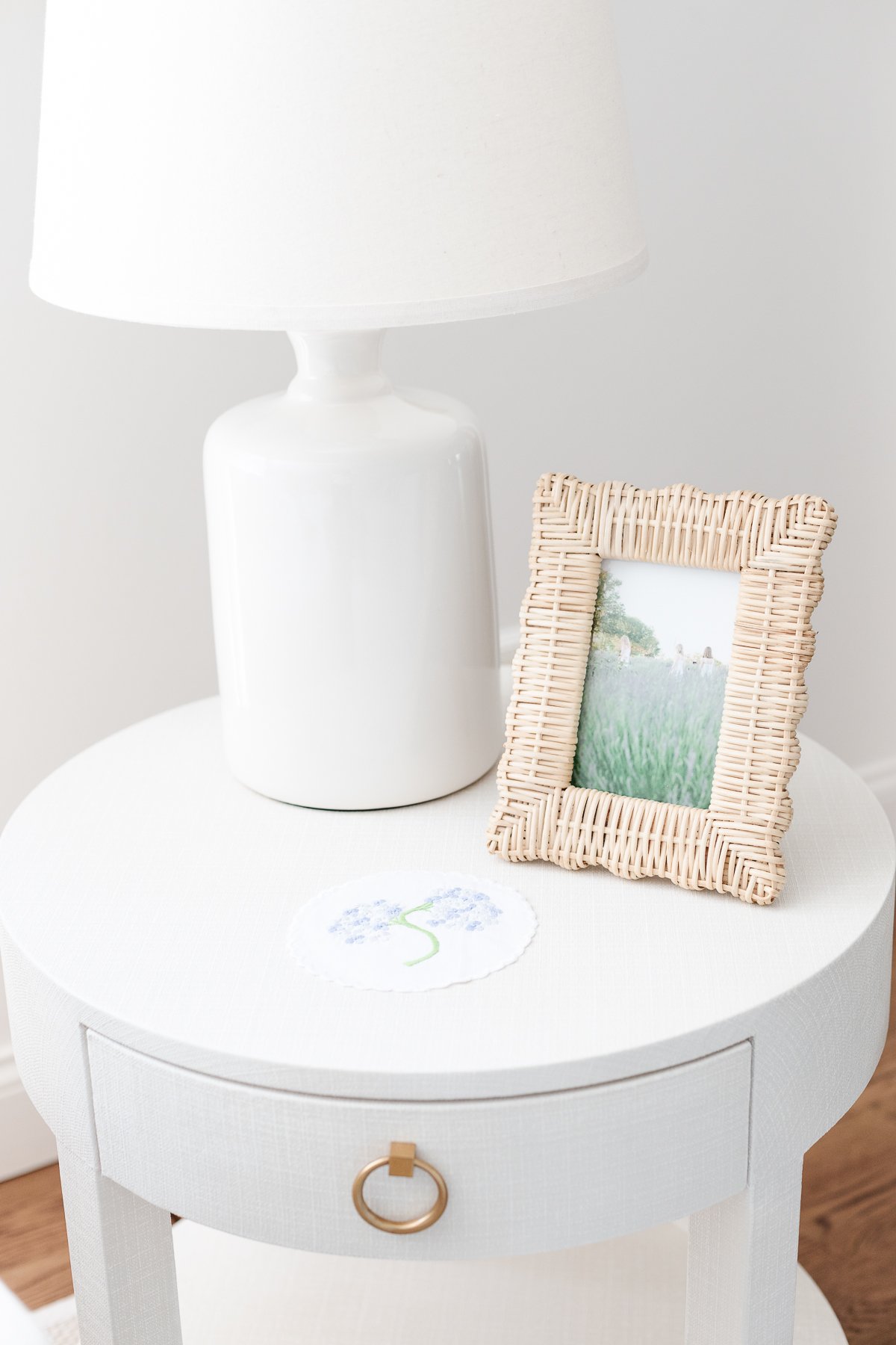 A decluttered white end table with a lamp and a picture on it.