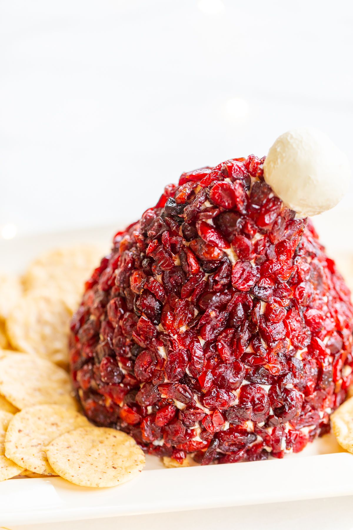 A cranberry cheeseball in the shape of a Santa's hat, on a plate surrounded by crackers.
