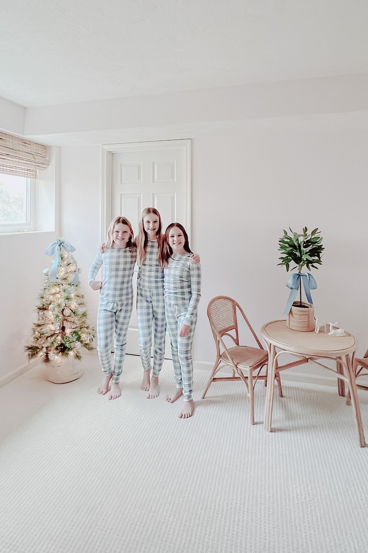 Three little girls in blue pajamas with a Christmas tree in the background.