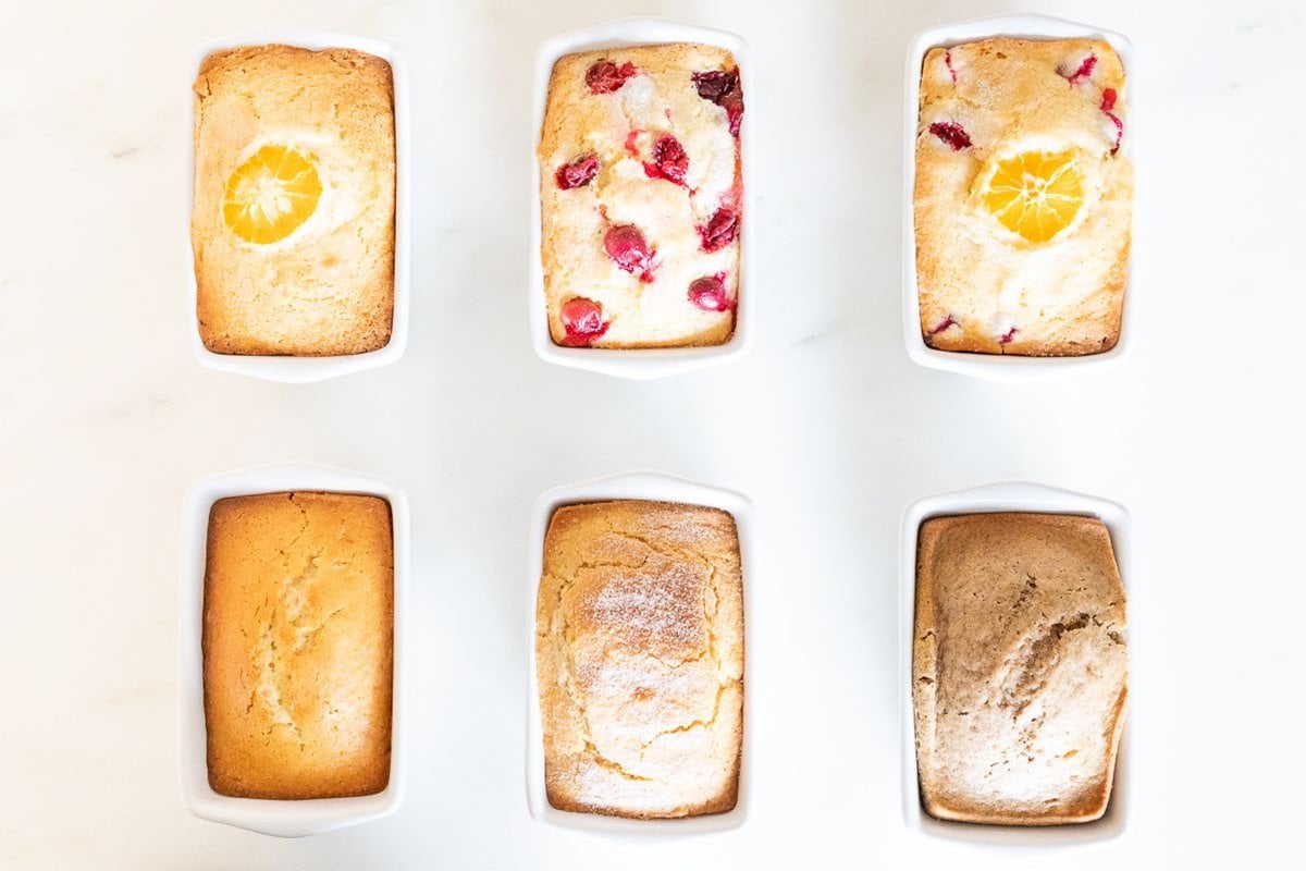 A variety of miniature loaves of quick bread recipes, baked into white ceramic loaf pans on a marble surface. 
