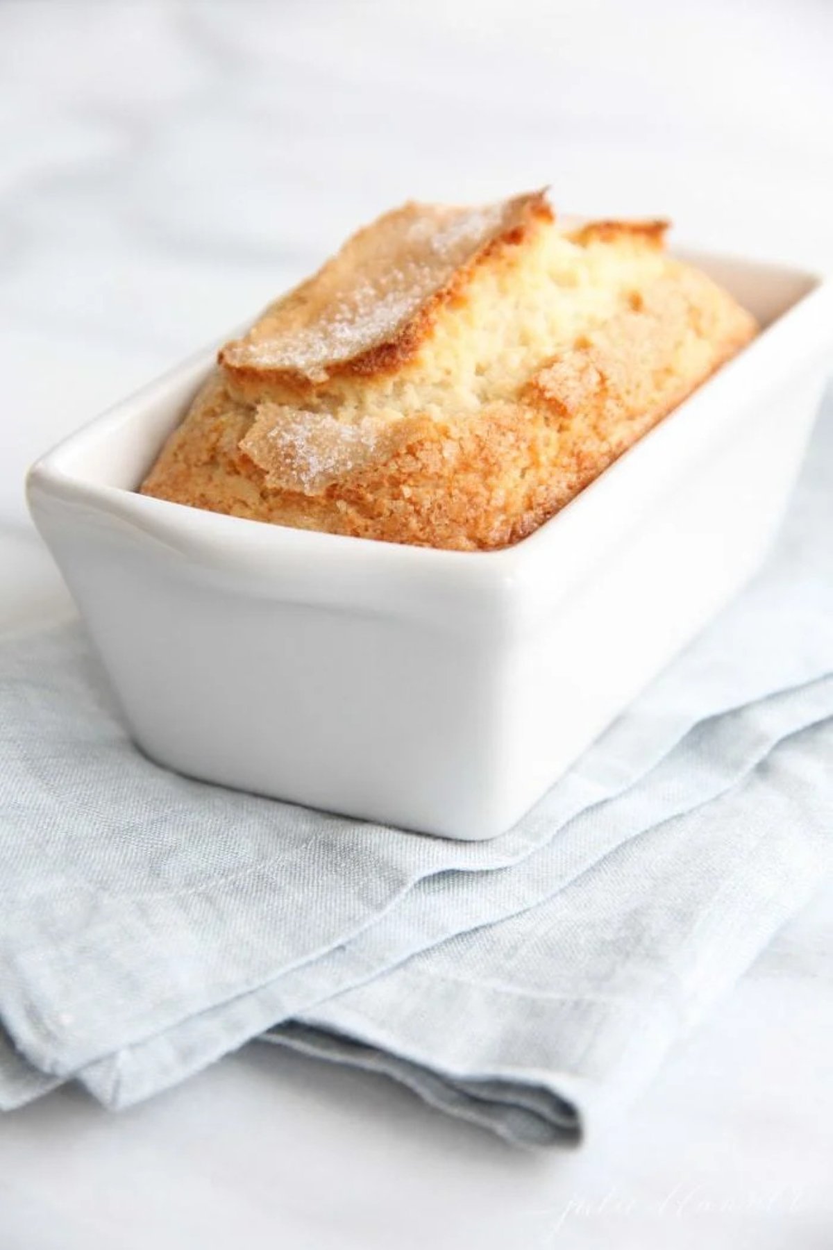 A loaf of sweet bread in a white ceramic mini loaf pan. 