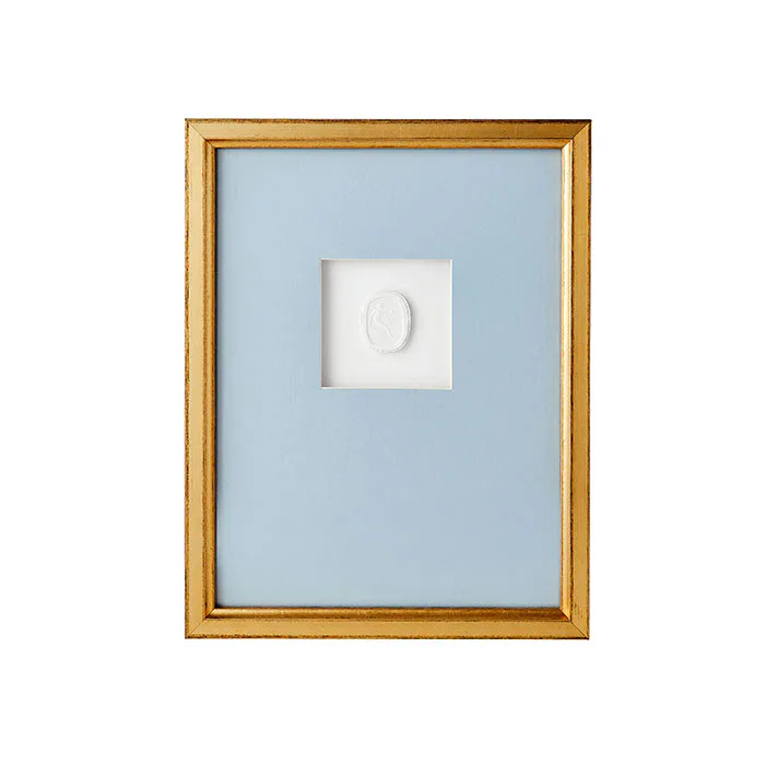 A gold-framed picture with a blue mat features a small white intaglio cameo centered in the middle.