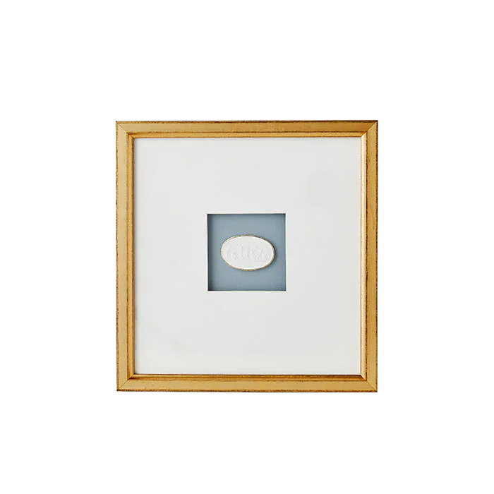 A gold-framed artwork featuring an intaglio—a small white oval object—centered on a blue background and surrounded by a wide white mat.