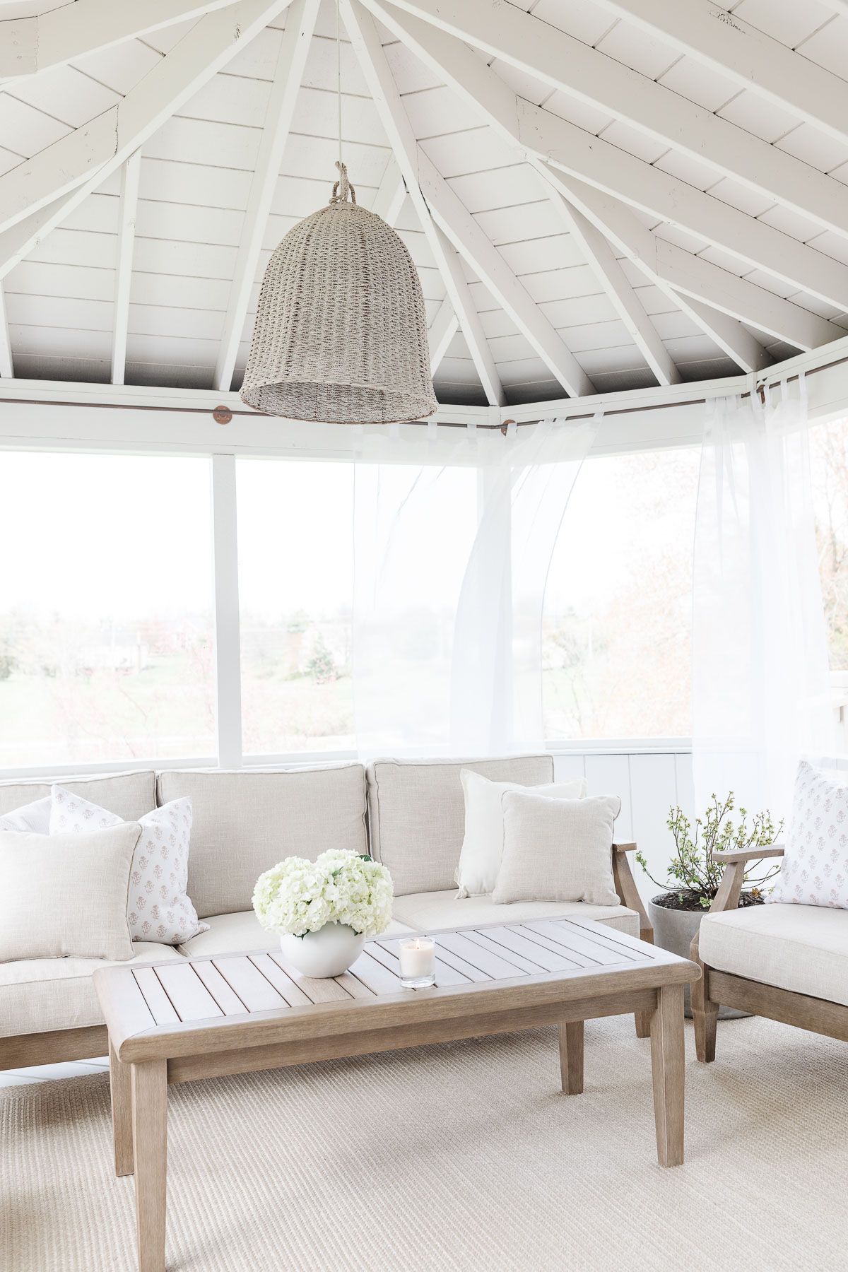 A screened in porch with light wood furniture. 