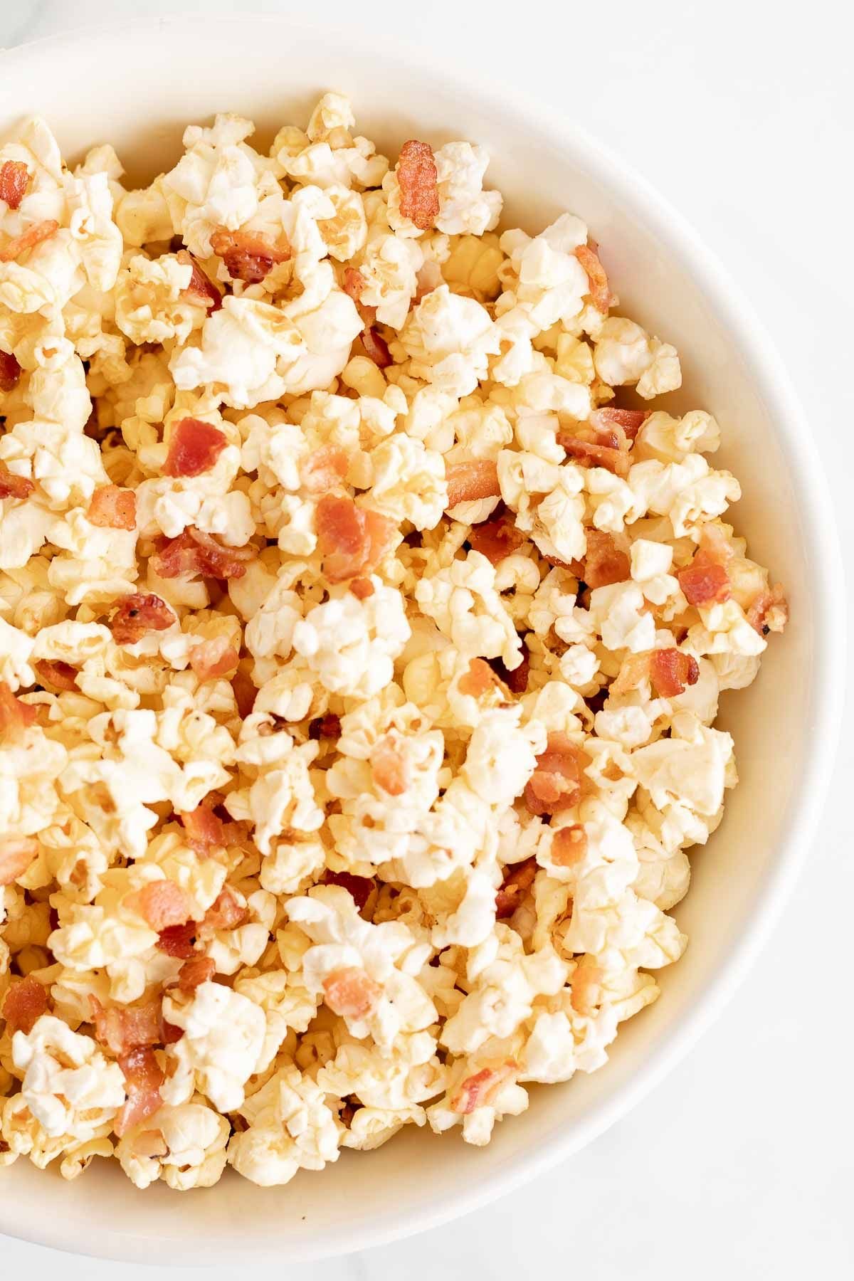 A white bowl filled with popcorn with bacon pieces