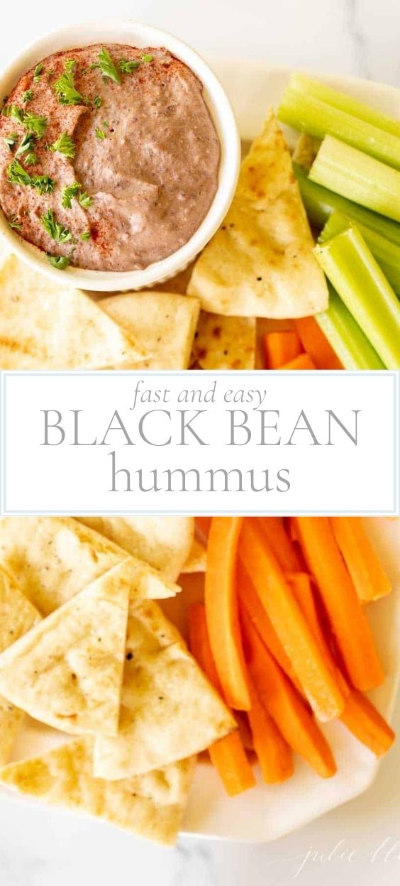 White bowl of black bean hummus with a platter of cut veggies and chips for dipping.