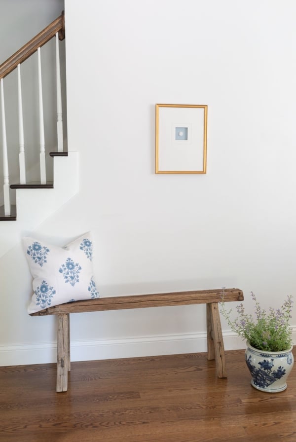 A wooden bench with a blue and white block print pillow in an entryway with wooden floors.