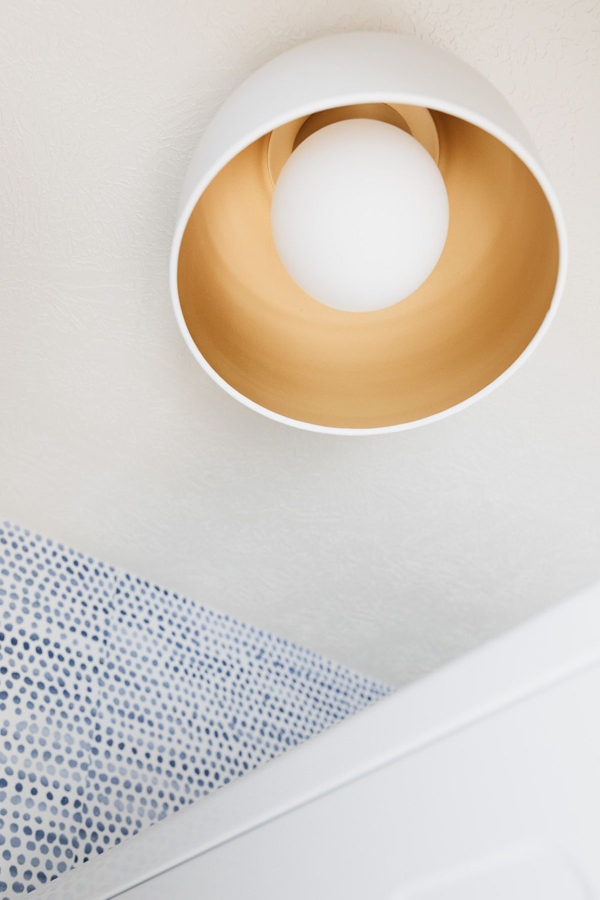 A modern gold flush mount light fixture near a blue and white polka dot wallpaper.