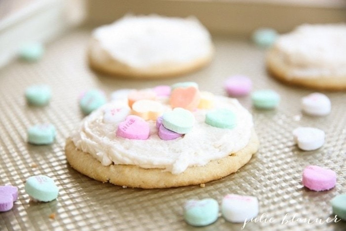 Sugar cookies topped with buttercream sugar cookie frosting and valentine heart candy. 