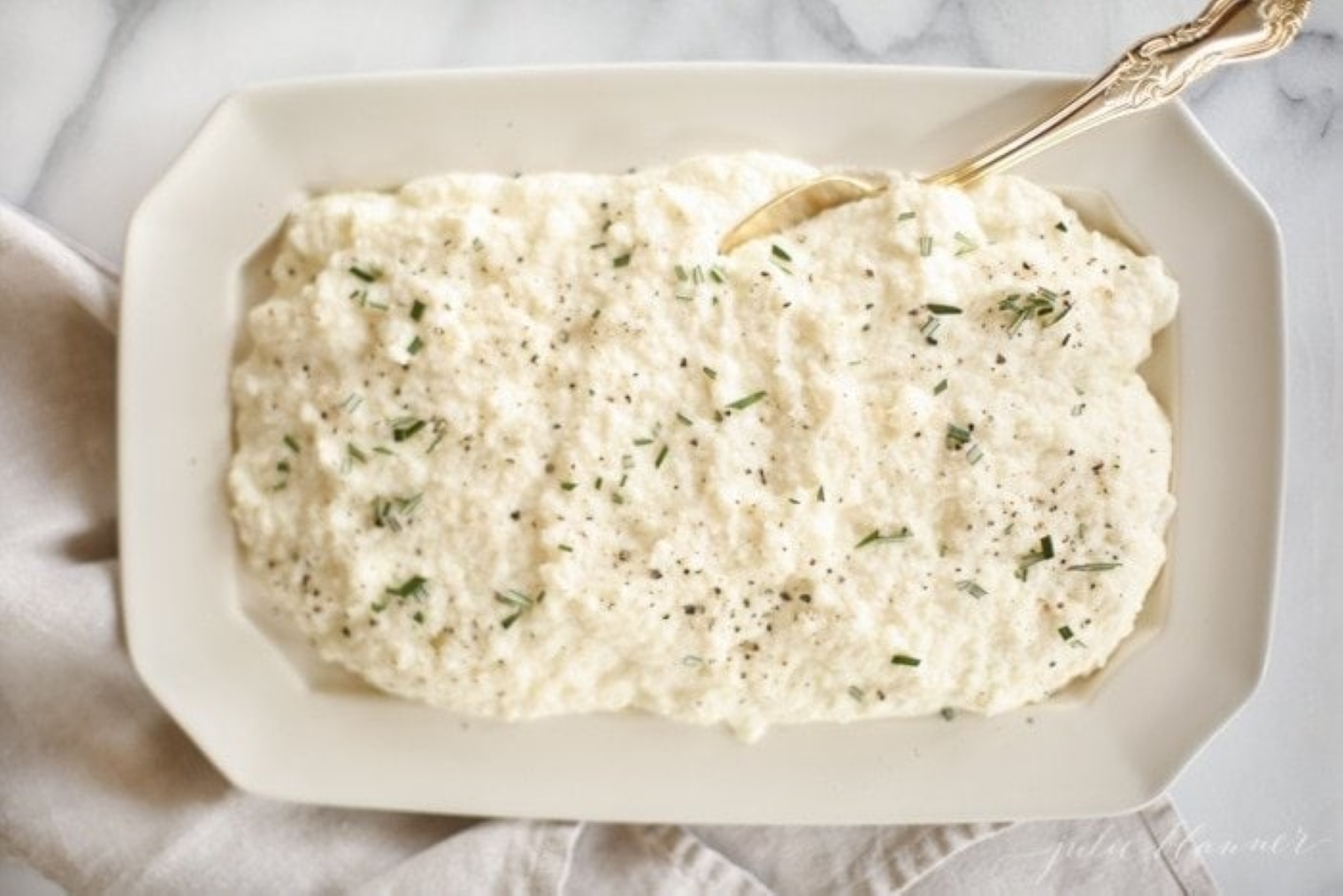 cauliflower mashed potatoes with rosemary in a white platter with gold spoon