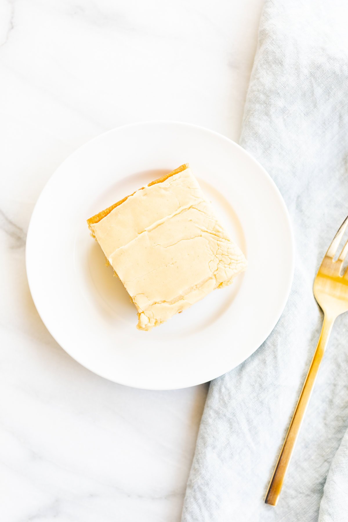 A slice of peanut butter cheesecake on a white plate beside a gold fork, set on a marble surface with a light gray cloth.