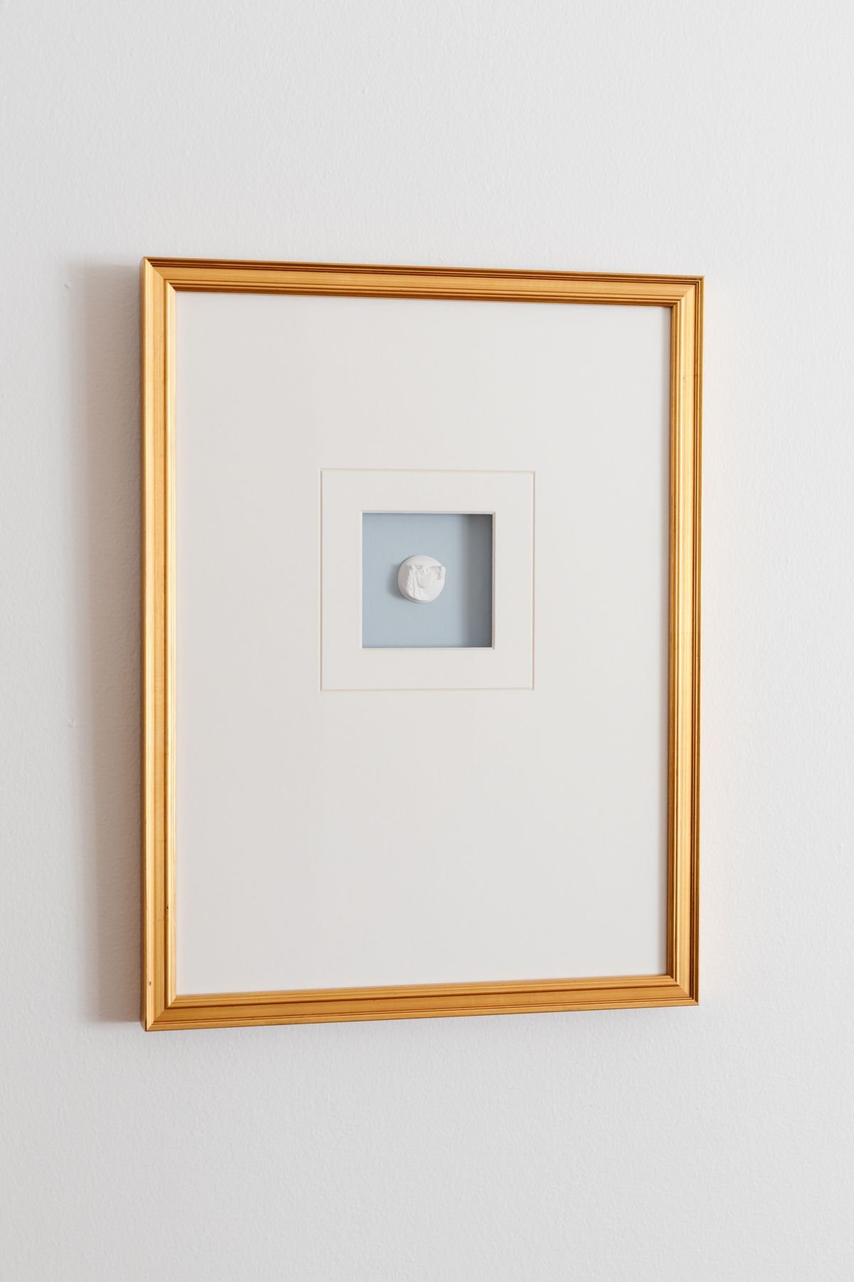 An intaglio art piece, framed with white matting and a gold frame. 