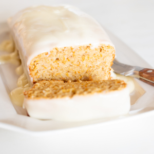 A slice of carrot bread with a homemade frosting recipe over the top, served on a white plate.