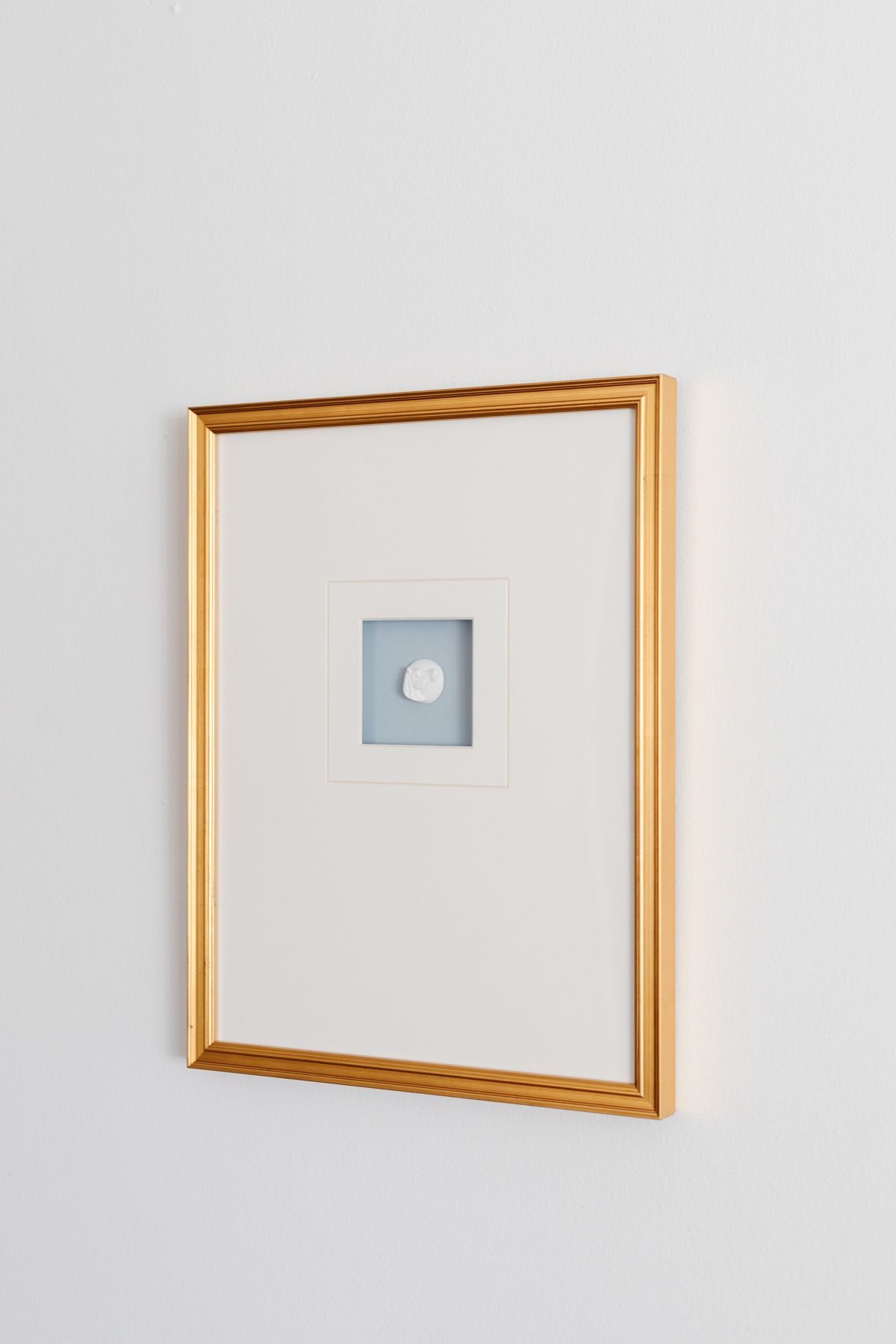 An intaglio art piece, framed with white matting and a gold frame.