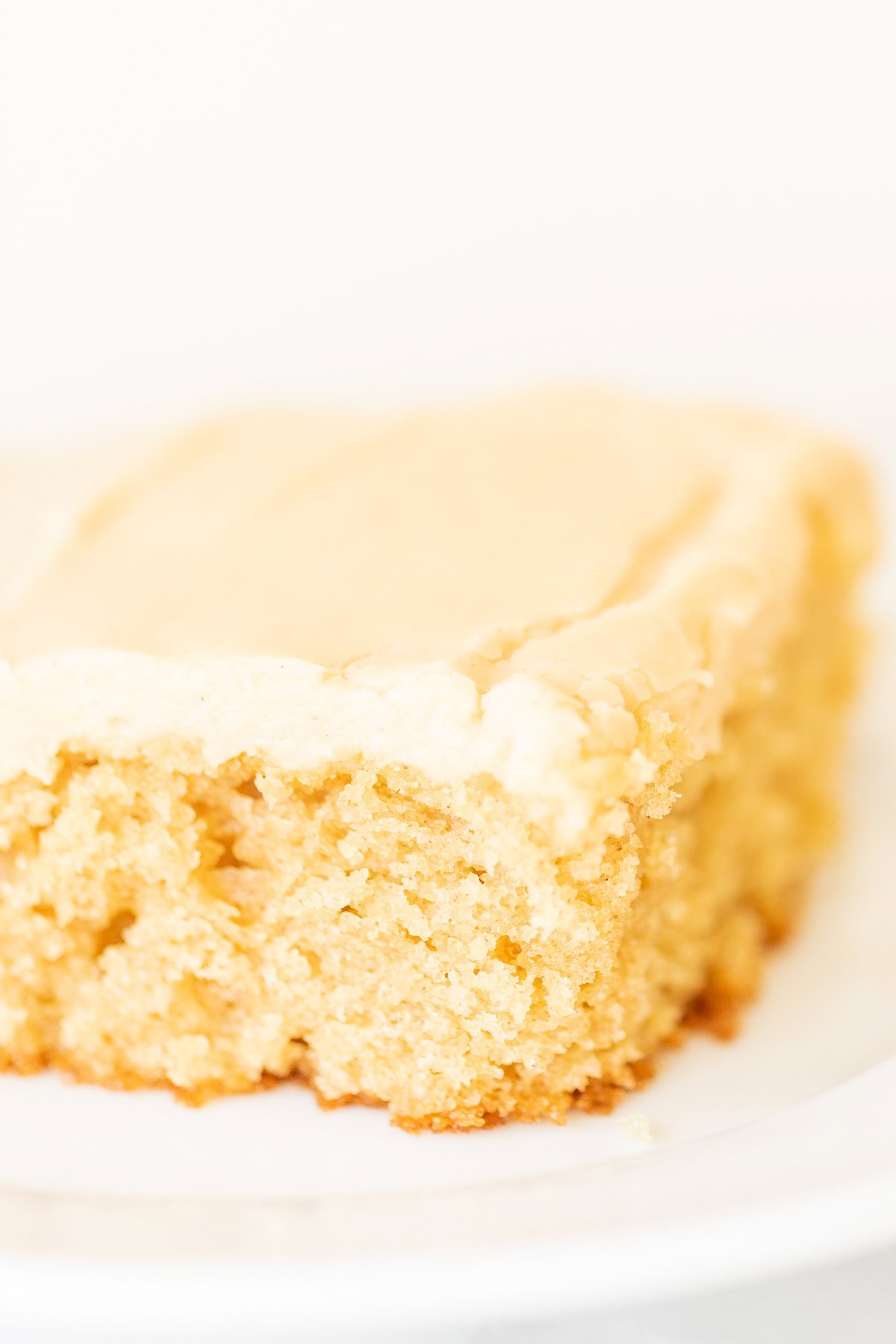 A close-up of a slice of moist peanut butter cake with a creamy top layer on a white plate.
