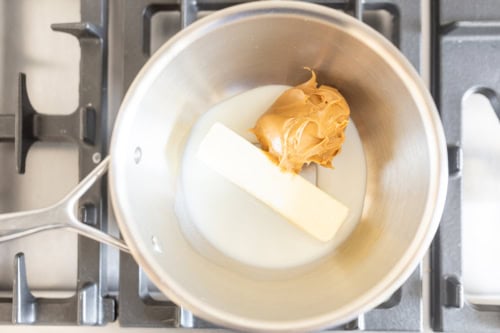 A saucepan on a stove containing milk, butter, and a dollop of peanut butter cake.