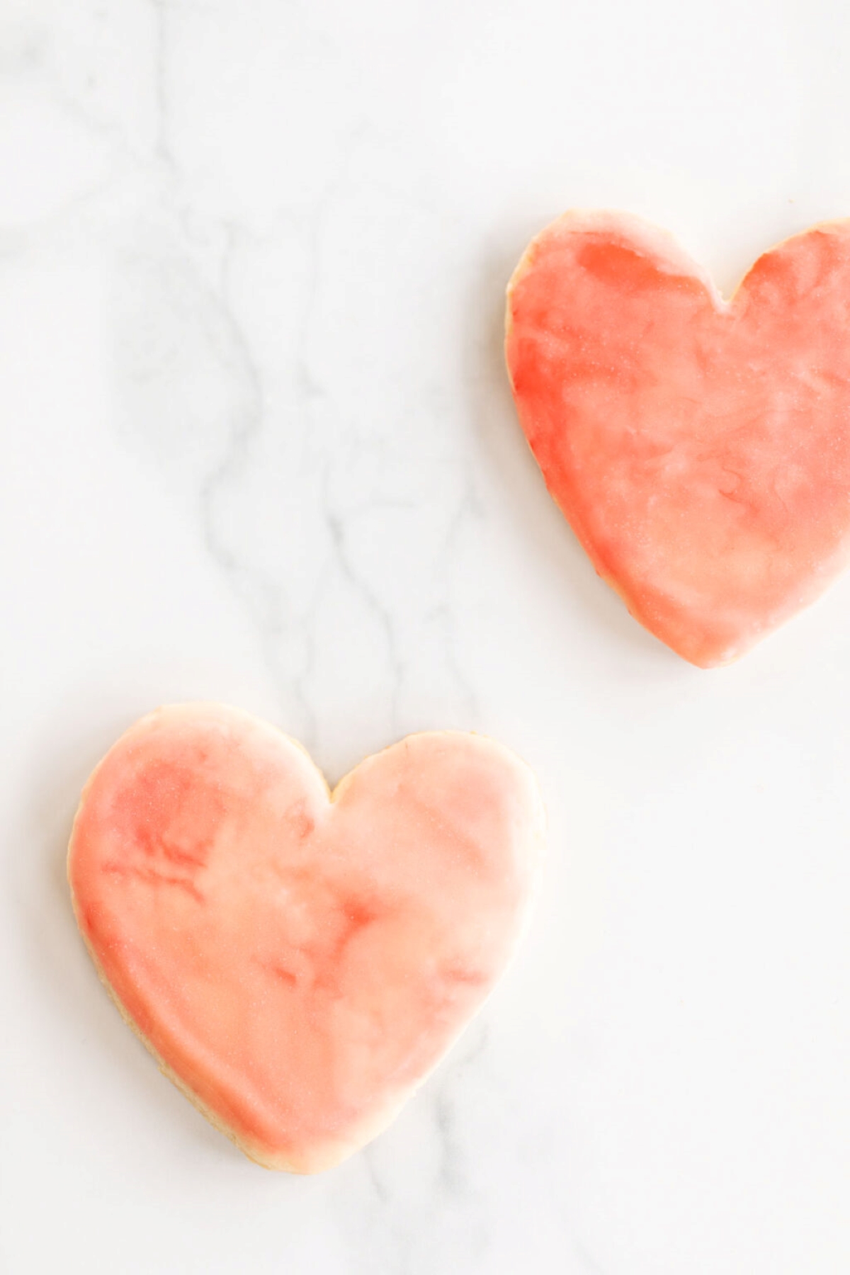 Pink sugar cookies in the shape of hearts, topped with royal icing. 
