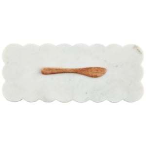 A white marble tray with scalloped decor and a wooden spoon on it.