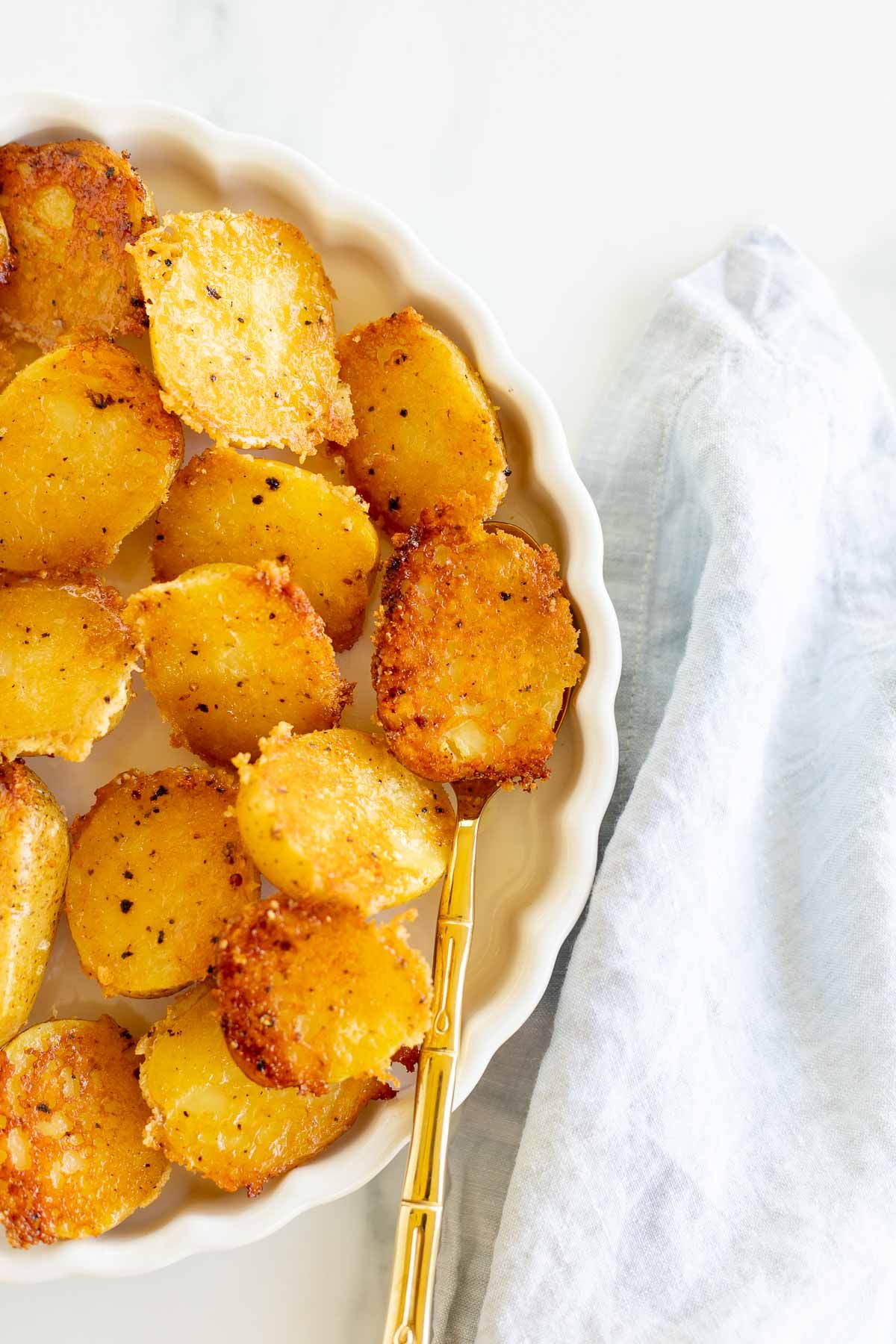 A white ruffled plate full of parmesan potatoes, with a small bowl of sour cream dip.