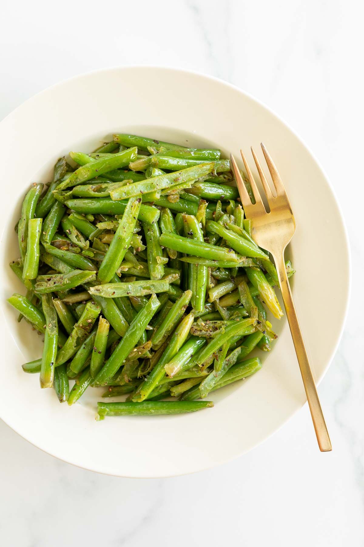 seasoned green beans in a white bowl on a marble countertop, in a guide to side dishes for chicken 