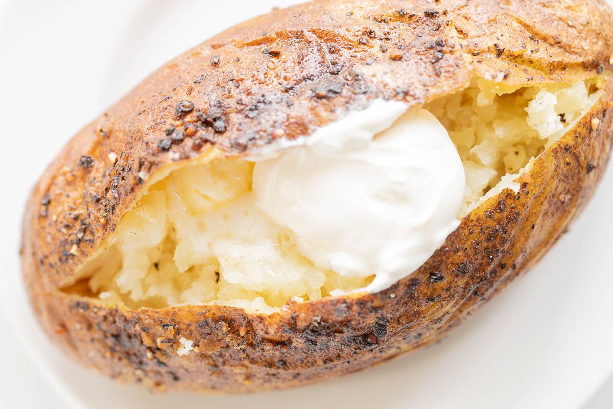 A grilled baked potato topped with butter and sour cream.