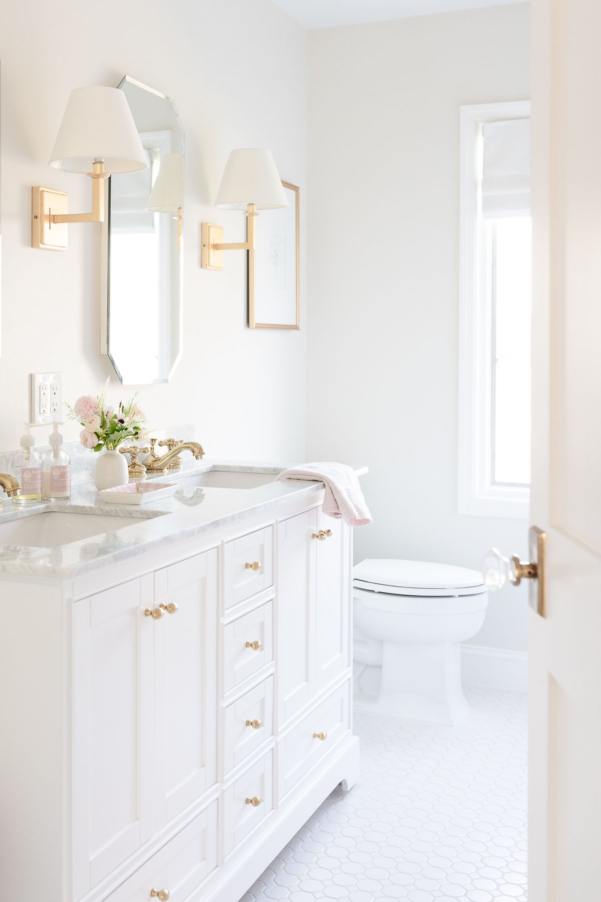 A white bathroom with gold hardware and soft pink accents. 