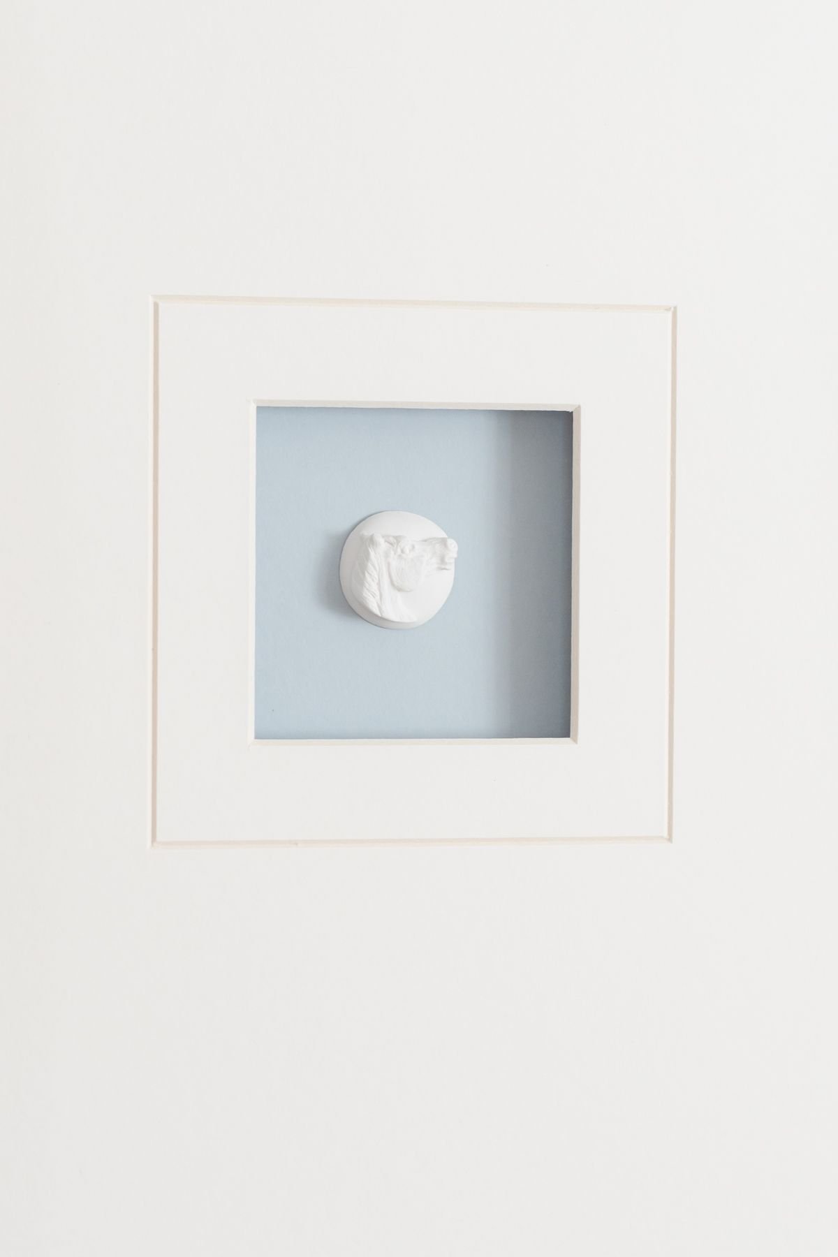 An intaglio art piece, framed with white matting and a blue background.