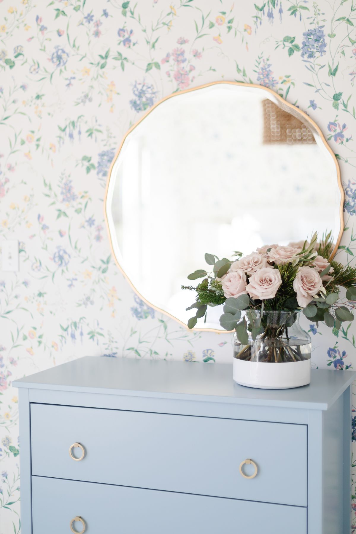 a blue dresser with an Amazon home mirror above, in a wallpapered bedroom
