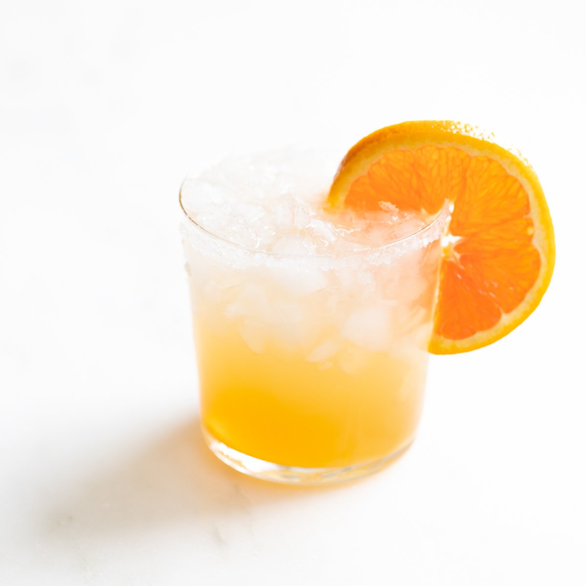 A glass of Cadillac margarita with crushed ice, garnished with an orange slice.