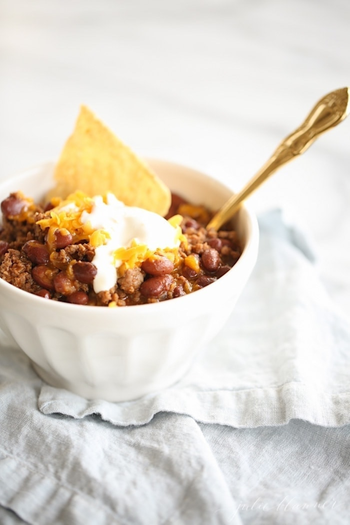 A white bowl of chili topped with sour cream and cheese. 