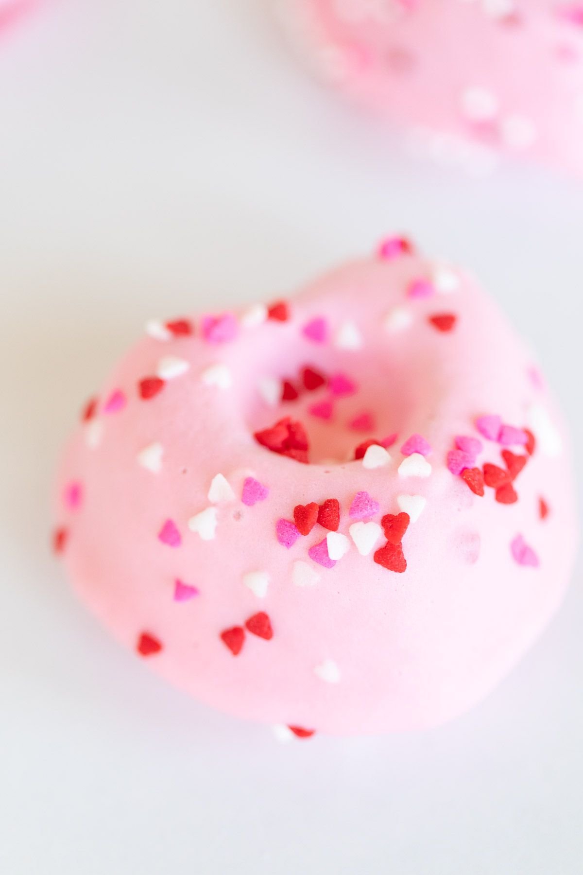 Heart shaped Valentine doughnuts on a white surface, covered in pink icing and sprinkles. 