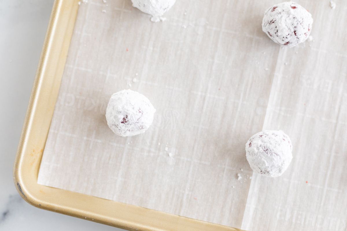 Red velvet gooey butter cookies dusted in powder sugar on a gold baking sheet.