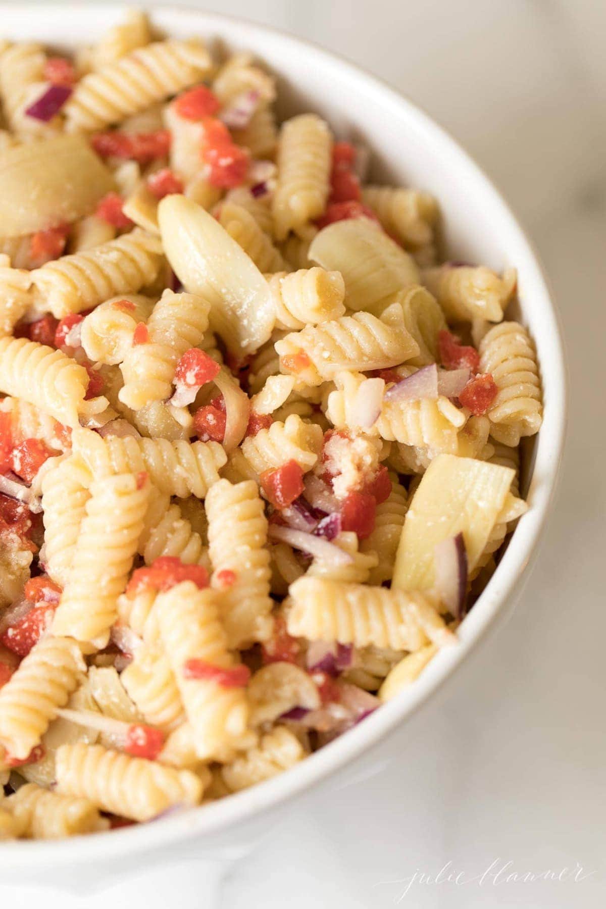A white bowl filled with Italian pasta salad. 