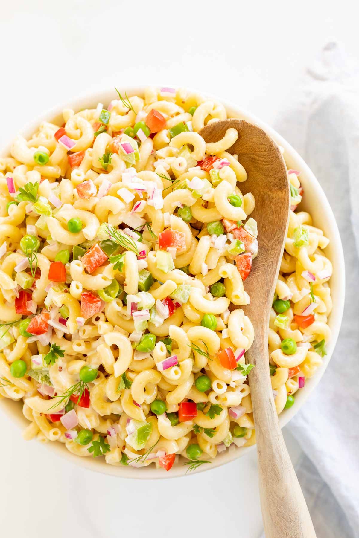 A large bowl full of macaroni salad with a wooden spoon for serving. 