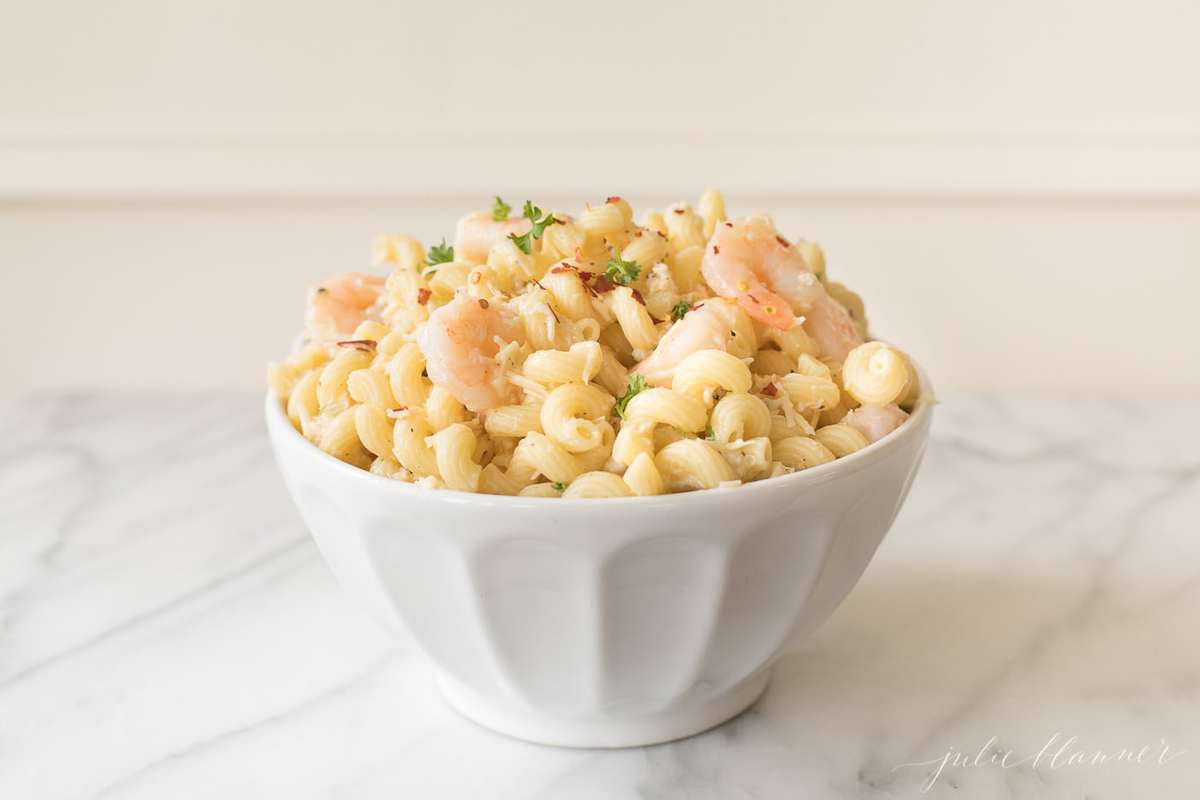 A white bowl on a marble countertop, filled with a seafood pasta salad recipe. 