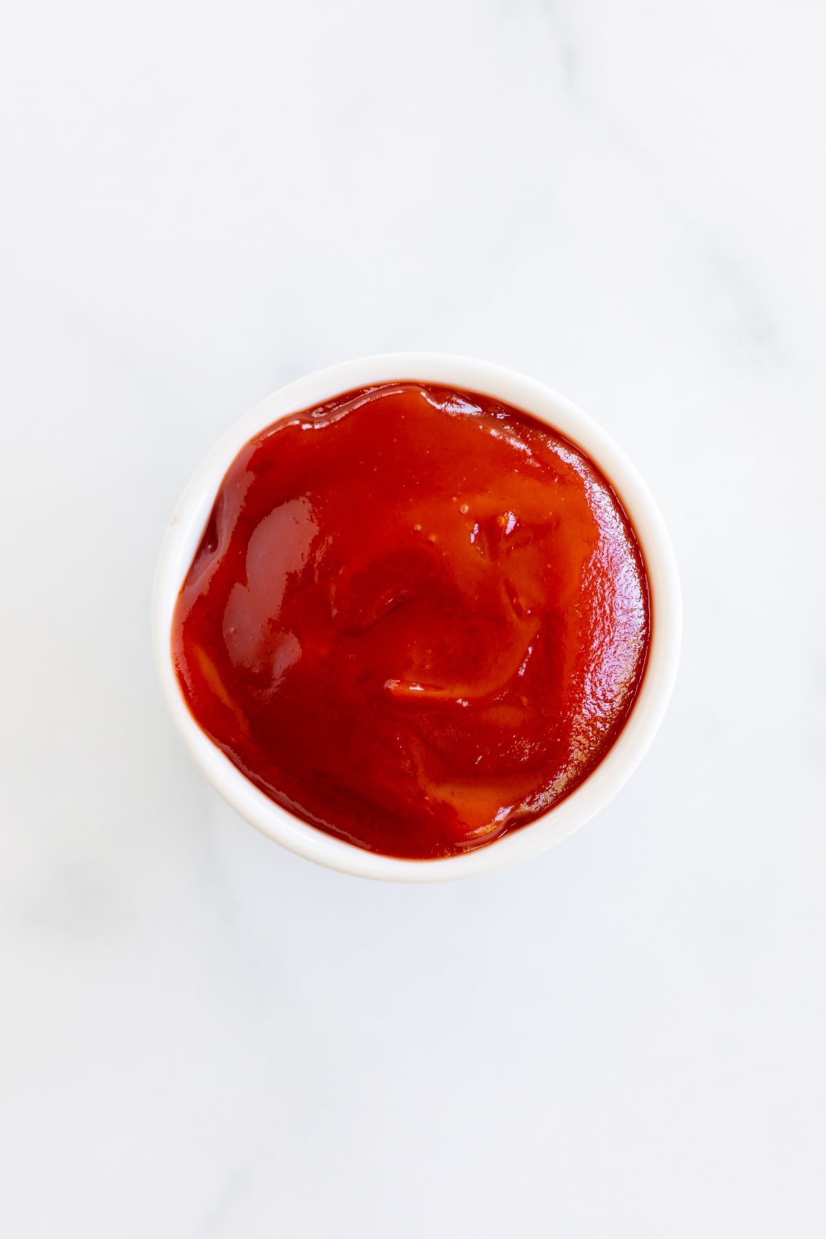 A small bowl of ketchup on a marble countertop, image is featured in a guide to tomato paste substitutes.
